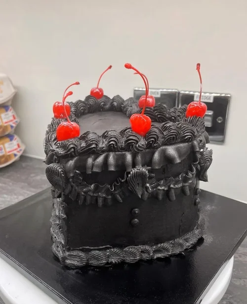Black heart-shaped birthday cake with red cherries
