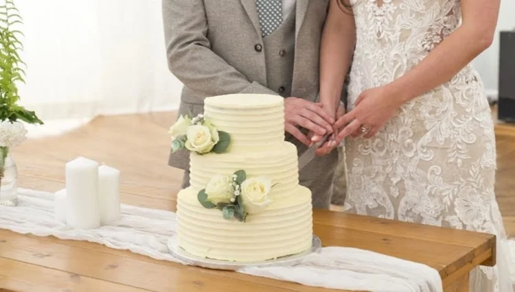 Three-tier white wedding cake with roses being cut